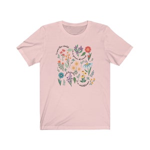 May include: Pink t-shirt with a floral design and the text "To see the world as a grain of sand and heaven in a wildflower."