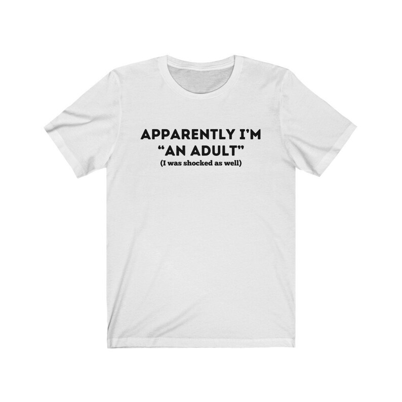 May include: White t-shirt with black text that reads "Apparently I'm "An Adult" (I was shocked as well)"