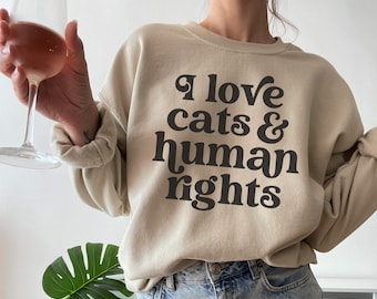 May include: A beige sweatshirt with the text "I love cats & human rights" printed in black.
