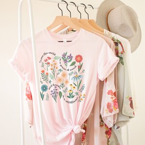 May include: Pink t-shirt with a floral design and the text "To see the world in a grain of sand and heaven in a wildflower."
