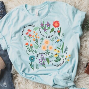 May include: A light blue t-shirt with a floral design and the text "To see the world in a grain of sand and heaven in a wildflower".