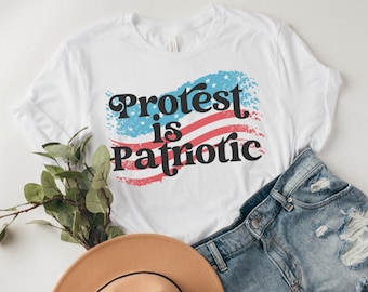 May include: White t-shirt with a distressed American flag design and the text "Protest is Patriotic" in black.