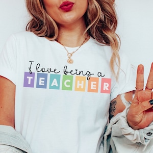 May include: White t-shirt with the text "I love being a TEACHER" in rainbow colored squares.