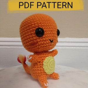 May include: Orange crocheted amigurumi toy of a Pokemon character with a yellow patch on its back and a flame-like tail. The toy has large black eyes and a smiling mouth.