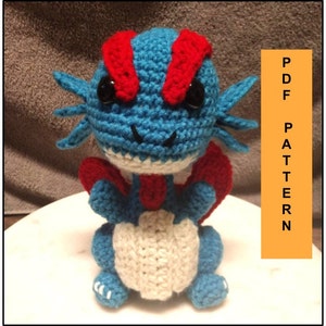 May include: Crocheted blue and red dragon amigurumi toy with white accents. The dragon has a toothy grin and large black eyes. PDF PATTERN.