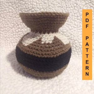 May include: A crocheted vase with a brown, white, and black color scheme. The vase has a wide mouth and a round body.