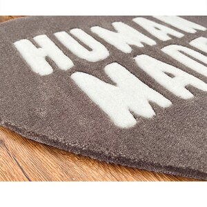 May include: A gray round rug with the words "HUMAN MADE" in white raised lettering.