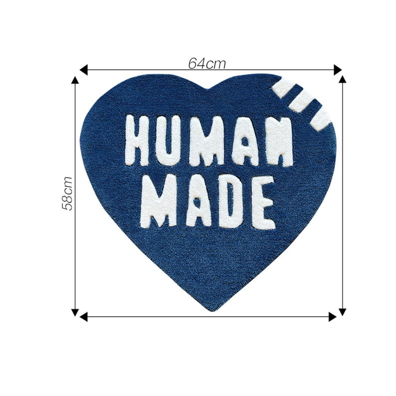 May include: A blue heart-shaped rug with the text "HUMAN MADE" in white lettering. The rug measures 64 cm by 58 cm.