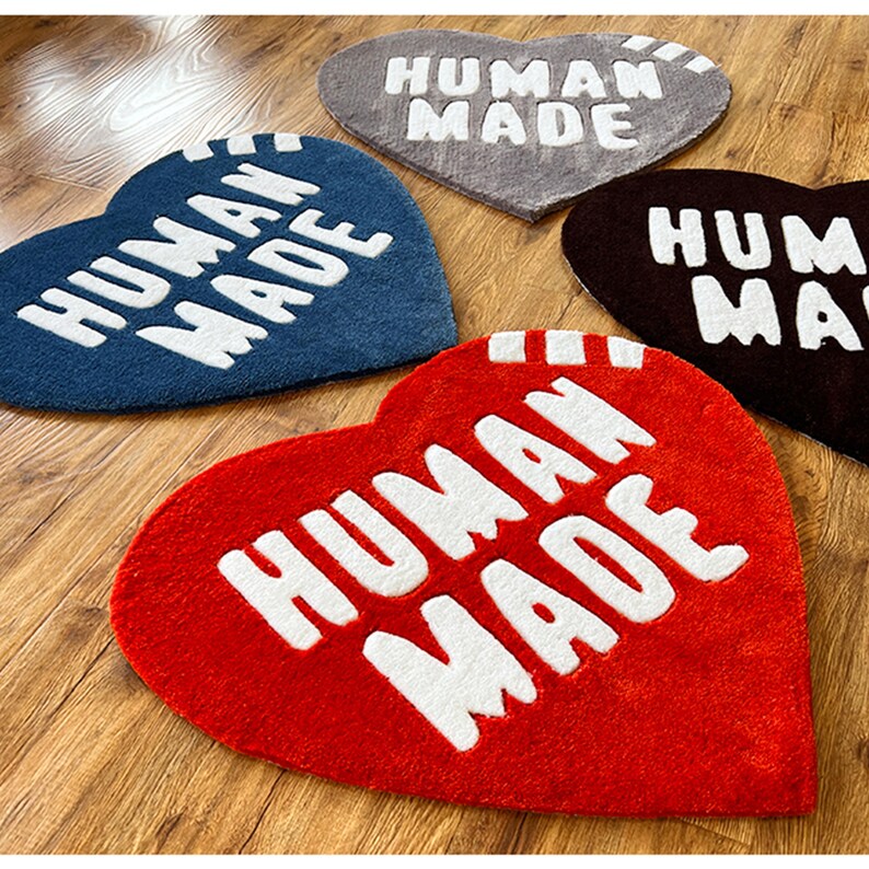 May include: Four heart-shaped rugs with the text "HUMAN MADE" in white lettering. The rugs are in red, blue, brown, and gray.