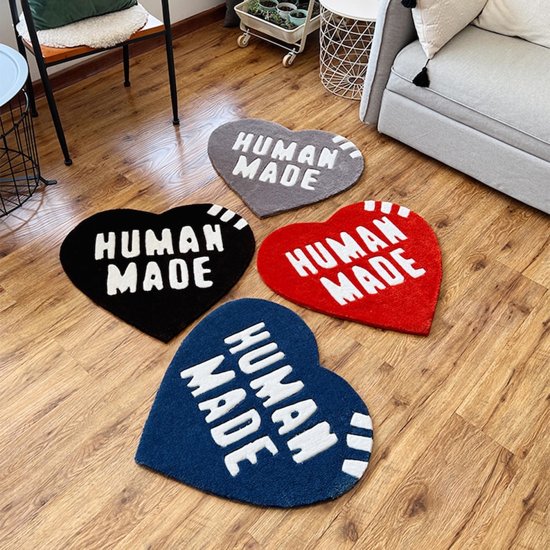 May include: Four heart-shaped rugs with the text "HUMAN MADE" in white lettering. The rugs are in gray, black, red, and blue.
