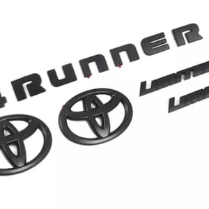 Könnte beinhalten: Ein Set aus mattschwarzen Auto-Emblemen, bestehend aus einem 4RUNNER-Schriftzug, zwei ovalen Toyota-Logos und zwei LIMITED-Plaketten. Jedes Teil hat eine kräftige, durchgehend schwarze Oberfläche mit klaren Kanten für die Außenanwendung.
