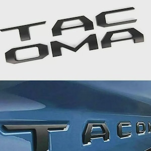 May include: A set of matte black individual letters spelling out TACOMA in a bold, angular font. The letters are shown both as separate pieces on a plain background and installed as a vehicle emblem on a blue metallic surface.