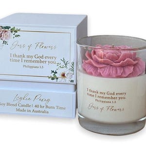 May include: A white soy blend candle with a pink flower on top. The candle is in a clear glass jar and has a label that says "Jars of Flowers" and "I thank my God every time I remember you. Philippians 1:3". The candle is also labelled "Lychee Peony" and has a burn time of 40 hours.