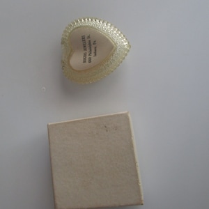 May include: A heart-shaped, clear plastic jewellery box with a scalloped edge and a white interior. The box has the text "ROGERS JEWELERS 660 Philadelphia St. Indiana, Pa." A small, beige cardboard box is also present.