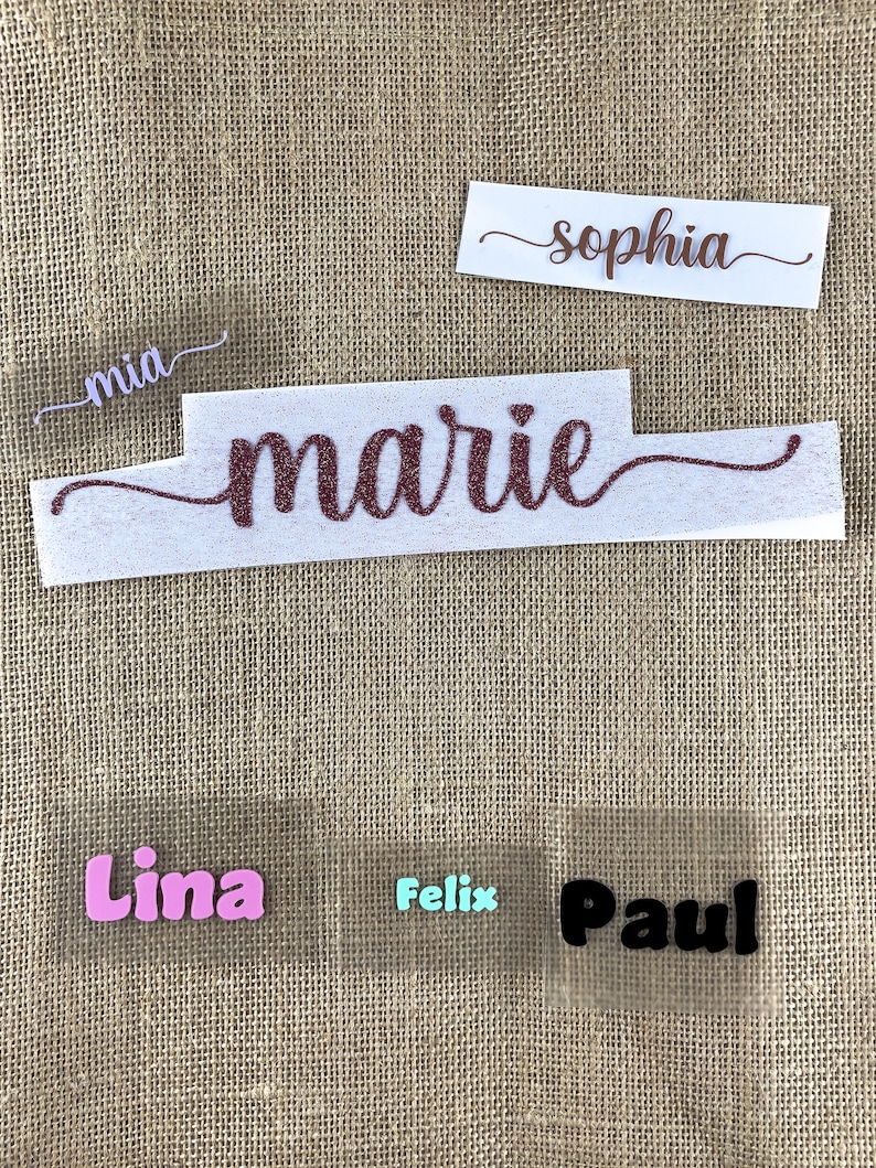 Op de afbeelding: Vijf strijklabels met verschillende namen. De namen zijn "mia", "marie", "sophia", "lima" en "paul". De labels zijn op een bruine jute achtergrond.