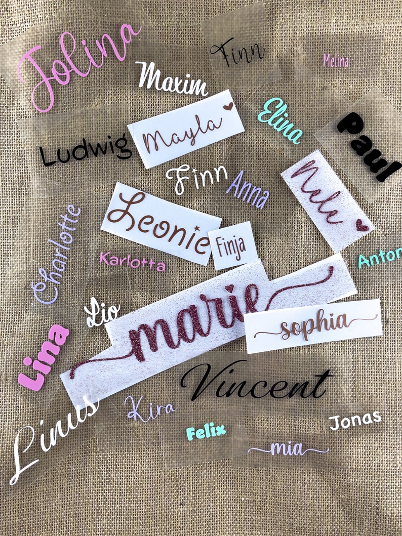 Op de afbeelding: Een verzameling gepersonaliseerde naamstickers met verschillende kleuren en lettertypen. De namen zijn Jolina, Maxim, Mayla, Finn, Elina, Ludwig, Leonie, Finja, Karlotta, Lina, Charlotte, Paul, Nele, Anna, Lio, Marie, Sophia, Vincent, Kira, Felix, Jonas en Mia.