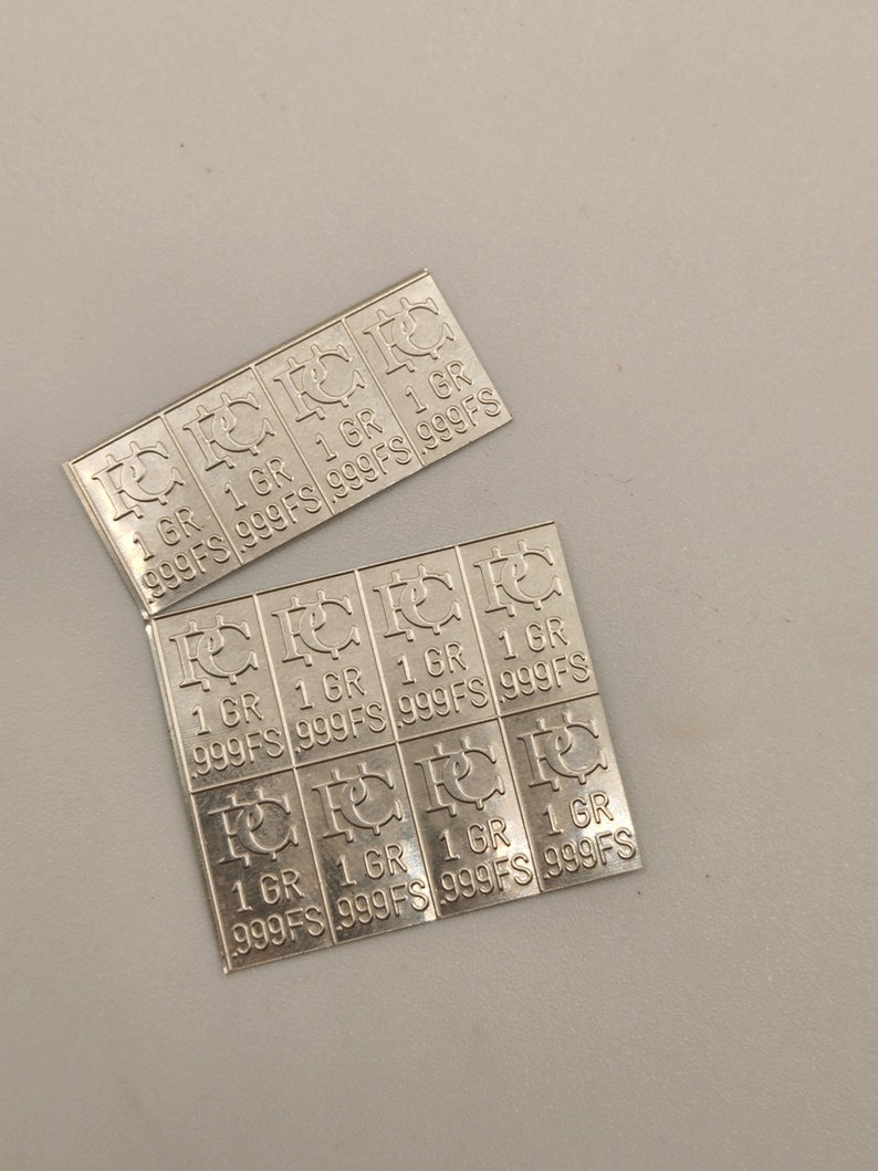 Puede incluir: Una l&aacute;mina de plata con m&uacute;ltiples secciones rectangulares, cada una con el texto "1 GR 999FS" repetido cuatro veces.