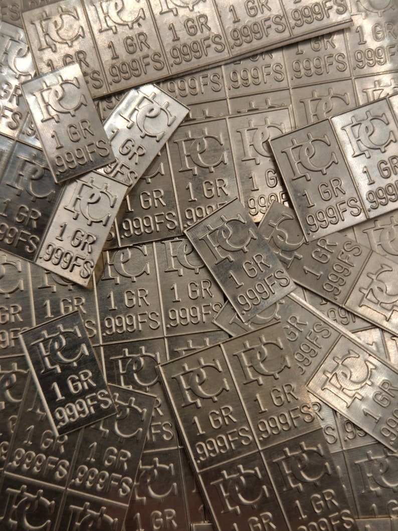 Peut inclure: Une pile de lingots d'argent, chaque lingot est estampill&eacute; "1 GR 999FS" et un symbole qui ressemble &agrave; une lettre stylis&eacute;e "C".