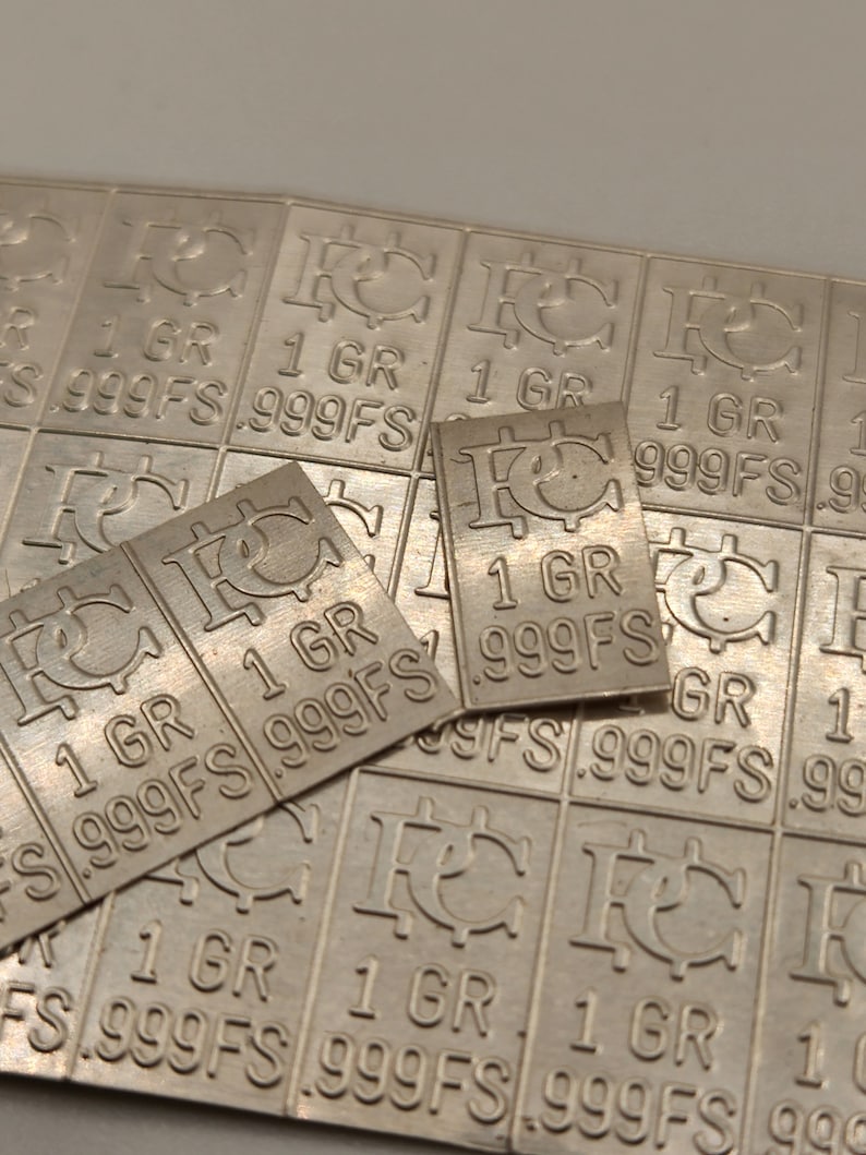 Op de afbeelding: Een close-up van een zilveren staaf met de inscriptie "1 GR 999FS" die meerdere keren wordt herhaald. De staven zijn in een rasterpatroon gerangschikt.