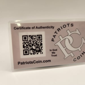 Puede incluir: Una tarjeta blanca con un certificado de autenticidad para una moneda de Patriots. La tarjeta presenta un c&oacute;digo QR en blanco y negro, el texto "Patriots Coin.com" y el texto "In God We Trust".