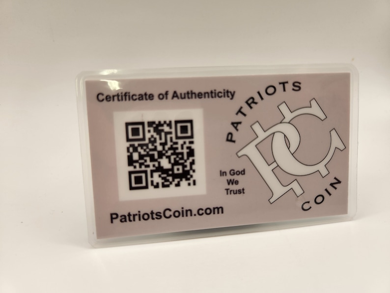 Puede incluir: Una tarjeta blanca con un certificado de autenticidad para una moneda de Patriots. La tarjeta presenta un c&oacute;digo QR en blanco y negro, el texto "Patriots Coin.com" y el texto "In God We Trust".