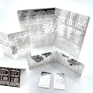 May include: A collection of silver bars, each stamped with "1 GR 999FS". The bars are arranged in a grid pattern, with some bars folded to show the inscription on both sides.