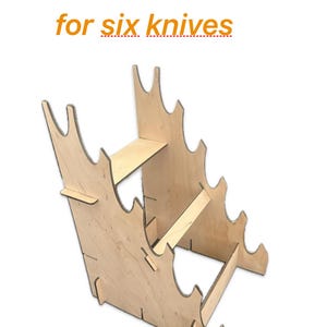 Puede incluir: Un soporte de madera para cuchillos diseñado para seis cuchillos. El soporte está hecho de madera de color claro y presenta un diseño escalonado con ranuras para cada cuchillo. El texto "KNIFE RACK for six knives" se muestra en naranja.