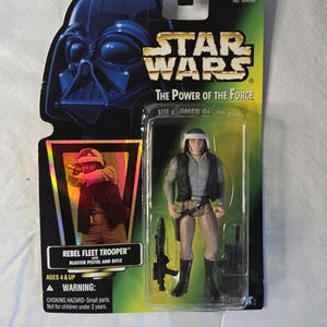 May include: Star Wars "The Power of the Force" action figure of a Rebel Fleet Trooper with blaster pistol and rifle. The figure is in a clear plastic case with a black and green Star Wars card featuring Darth Vader.