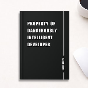 May include: Black notebook with the text "PROPERTY OF DANGEROUSLY INTELLIGENT DEVELOPER" in white. The name "JOHN SMITH" is printed vertically on the right side. A white computer mouse and a cup of coffee are in the background.