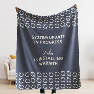 May include: A navy blue fleece blanket with a white repeating pattern of arrows. The blanket has white text that reads "System Update in Progress John is Installing Warmth".