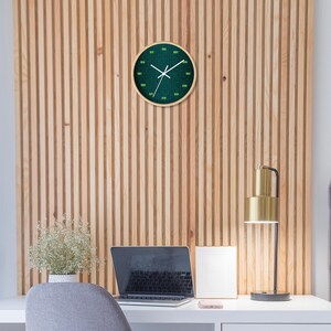 K&ouml;nnte beinhalten: Eine runde Wanduhr mit gr&uuml;nem Zifferblatt und wei&szlig;en Zeigern h&auml;ngt an einer Wand mit Holzlatten. Die Uhr hat einen hellen Holzrahmen. Ein Schreibtisch mit Laptop, Lampe und Blumenvase befindet sich im Vordergrund.