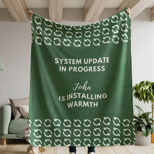 May include: A green blanket with white arrow symbols and the text "SYSTEM UPDATE IN PROGRESS" and "John IS INSTALLING WARMTH". The blanket is held up by a person.