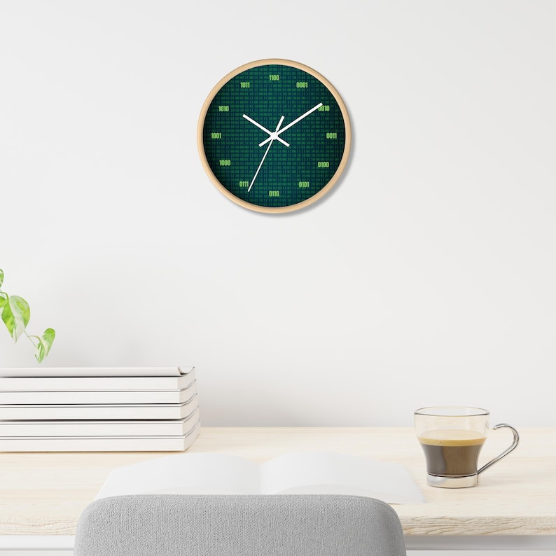 K&ouml;nnte beinhalten: Runde Wanduhr mit Holzrahmen. Das Zifferblatt ist dunkelblaugr&uuml;n mit einem Muster aus gr&uuml;nem Bin&auml;rcode. Wei&szlig;e Zeiger zeigen die Uhrzeit an. Die Uhr h&auml;ngt an einer wei&szlig;en Wand.