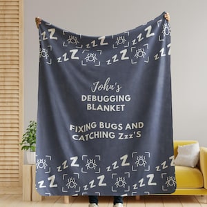 May include: A navy blue fleece blanket with a white bug and "zzz" pattern. The blanket has the text "John's Debugging Blanket Fixing Bugs and Catching Zzz's" printed in white.