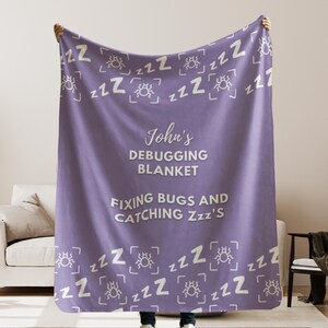 May include: Purple fleece blanket with a white bug and Z's pattern. The text "John's Debugging Blanket Fixing Bugs and Catching Zzz's" is printed in white on the blanket.