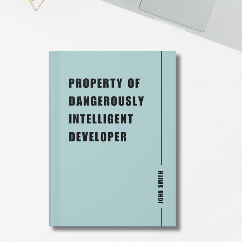 May include: A pale blue notebook featuring the words "PROPERTY OF DANGEROUSLY INTELLIGENT DEVELOPER" in black. The name "JOHN SMITH" is printed vertically on the right side of the notebook.