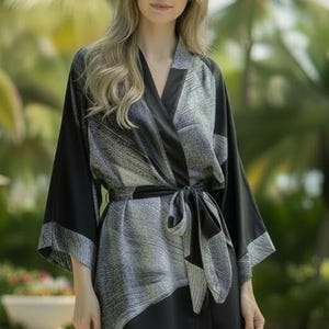 Puede incluir: Bata con estampado negro y gris con cinturón a juego. La bata tiene mangas anchas y un diseño envolvente. La tela tiene un brillo sutil y el estilo general es elegante y cómodo.