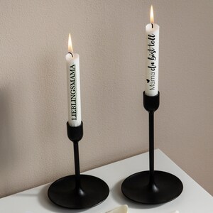 May include: Two black candle holders with white candles. The candle on the left says "LIEBLINGSMAMA" and the candle on the right says "Mama du bist toll" with a small heart symbol.