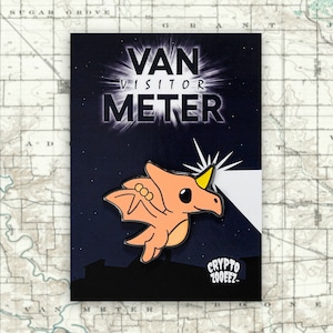May include: A pink and yellow enamel pin featuring a cartoon creature with wings and a horn. The pin says "Van Visitor Meter" and "Crypto Zooeez" at the bottom.