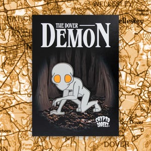 May include: A black rectangular pin featuring the text "THE DOVER DEMON" in white. The pin depicts a gray, humanoid creature with orange eyes crawling in a forest setting. The text "CRYPTO 200EEZ" is also visible.
