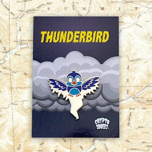 May include: A blue and white cartoon bird with outstretched wings, flying through a gray cloud. The bird has a red beak and white eyes. The text "THUNDERBIRD" is in yellow letters at the top of the image. The text "CRYPTO ZOOEEZ" is at the bottom of the image.
