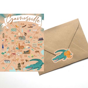 May include: A colorful illustrated map of Gainesville, Florida, with a brown envelope and a sticker of a green alligator with orange slices. The map features landmarks and points of interest, including the University of Florida, the Swamp, and the Hippodrome Theatre.
