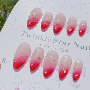 May include: Set of ten oval-shaped false nails with a red and white ombre design. The nails have gold flakes embedded in the white portion of the design. The nails are arranged on a white card with the text "Twinkle Star Nail" and "To the best of you".