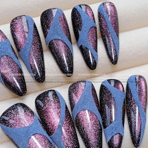 May include: A set of almond-shaped press-on nails featuring a deep purple cat-eye magnetic shimmer finish contrasted by matte blue textured diagonal stripes. The nails display a glossy, reflective surface with a distinct grainy, sand-like texture.