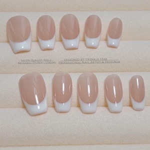 Pode incluir: Um conjunto de unhas postiças com um design clássico de manicure francesa. Cada unha apresenta uma base de cor nude com uma ponta branca. O texto na imagem diz: "SALON QUALITY NAILS... DESIGNED BY TWINKLE STAR... REUSABLE! STURDY! STRONG! PROFESSIONAL NAIL ARTIST & DESIGNER."