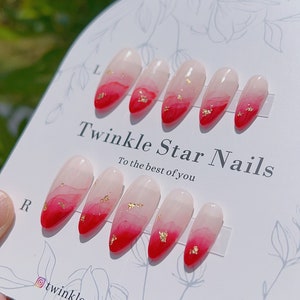 May include: Set of ten red and white ombre press-on nails with gold flakes. The nails are displayed on a white card with the text "Twinkle Star Nails, to the best of you" and the Instagram handle "@twinklestarnailslab".