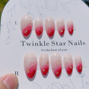 May include: Set of ten false nails with a pink and red ombre design and gold glitter accents. The nails are arranged on a white card with the text "Twinkle Star Nails To the best of you" and the Instagram handle "@twinklestarnailslab".