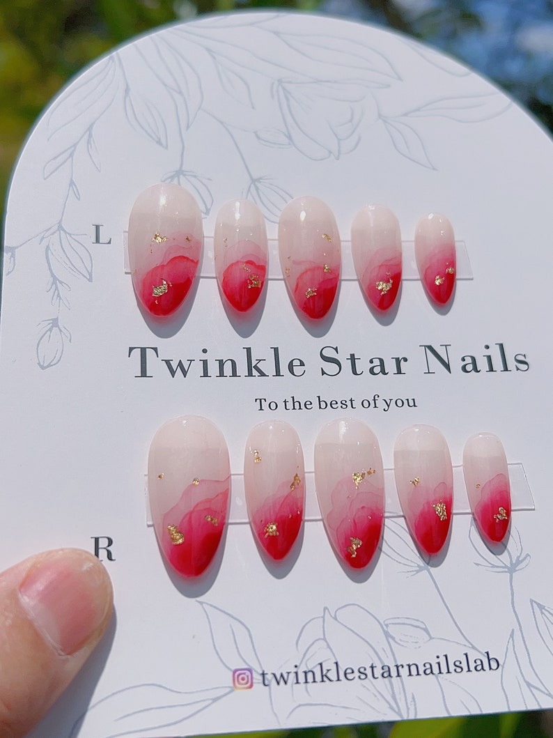 May include: Set of ten false nails with a pink and red ombre design and gold glitter accents. The nails are arranged on a white card with the text "Twinkle Star Nails To the best of you" and the Instagram handle "@twinklestarnailslab".
