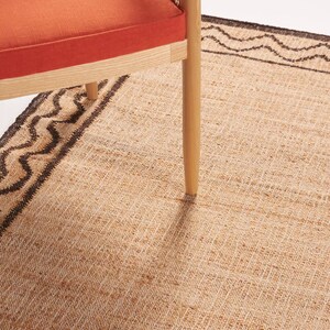 May include: A woven jute rug with a brown border pattern. A wooden chair with a woven cane back and orange cushion sits on the rug.