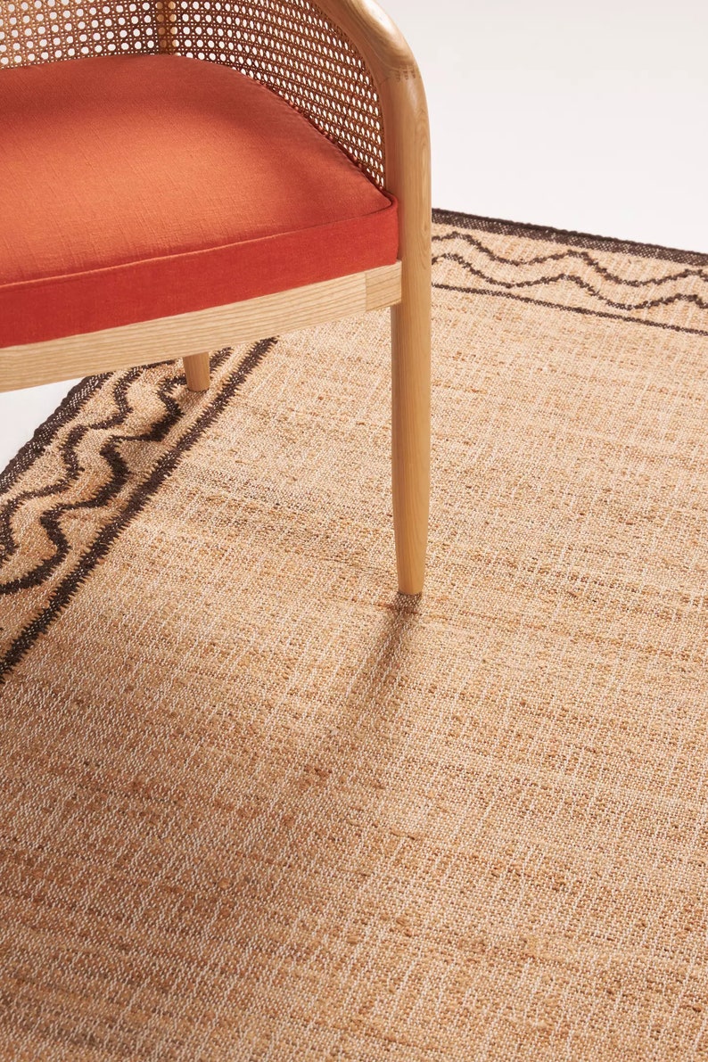 May include: A woven jute rug with a brown border pattern. A wooden chair with a woven cane back and orange cushion sits on the rug.
